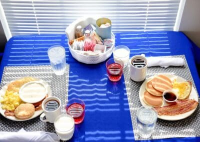 Delicious breakfast plates at Charter Senior Living of Paris, featuring pancakes, bacon, scrambled eggs, biscuits, and beverages on a table with a blue tablecloth.