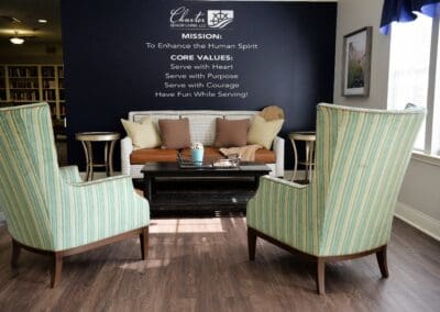 Comfortable seating area with striped armchairs and a sofa, featuring Charter Senior Living of Paris mission and core values on a navy accent wall.