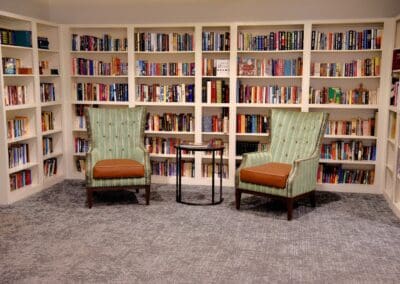 Cozy reading area with two armchairs and bookshelves filled with colorful books at Charter Senior Living of Paris.