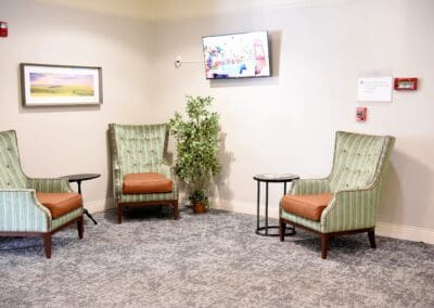Comfortable lounge area with three green-striped armchairs, a TV, and indoor plants at Charter Senior Living.