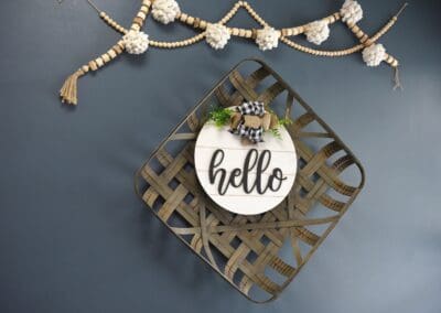 Decorative wall art featuring a woven basket and a 'hello' sign with a bow and greenery at Charter Senior Living of Paris.