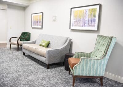 Seating area at Charter Senior Living of Paris featuring a modern sofa, armchairs, and scenic forest artwork on the walls.