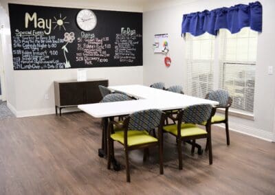 Activity room at Charter Senior Living with a May events calendar, modern chairs, and community tables.