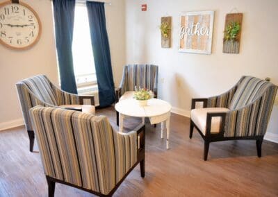 Comfortable sitting area at Charter Senior Living with striped armchairs around a white round table and 'Gather' wall décor.