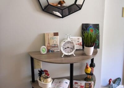 Decorative shelf with Paris-themed books, a white clock, rooster figurines, and a modern geometric mirror on the wall.