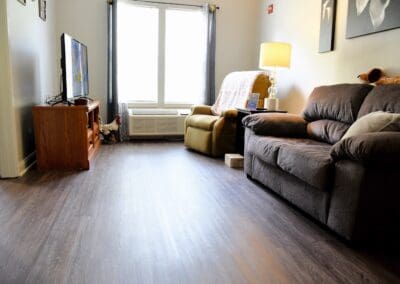 Cozy living room with a sofa, armchair, TV stand, and large window at Charter Senior Living of Paris.