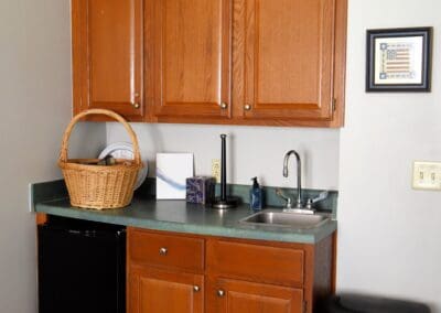 Kitchenette area at Charter Senior Living of Paris, TN, featuring wood cabinets, a small sink, mini fridge, and decorative rooster accents