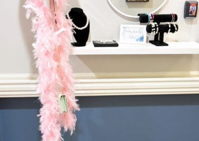 Pink cowboy hat and feather boa on a stand next to a vanity area with jewelry displays and a round mirror.