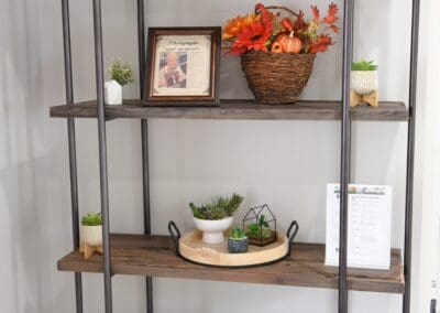 Decorative shelving unit with framed photos, plants, and autumn-themed floral arrangements at Charter Senior Living of Paris.