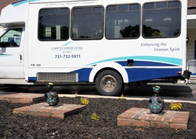 Charter Senior Living of Paris, TN transportation bus parked outside the community, with decorative garden statues in the foreground